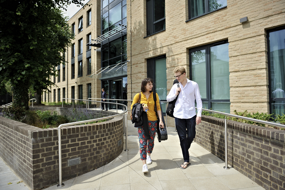 Two students walking outside a modern brick building, carrying their instrument cases.